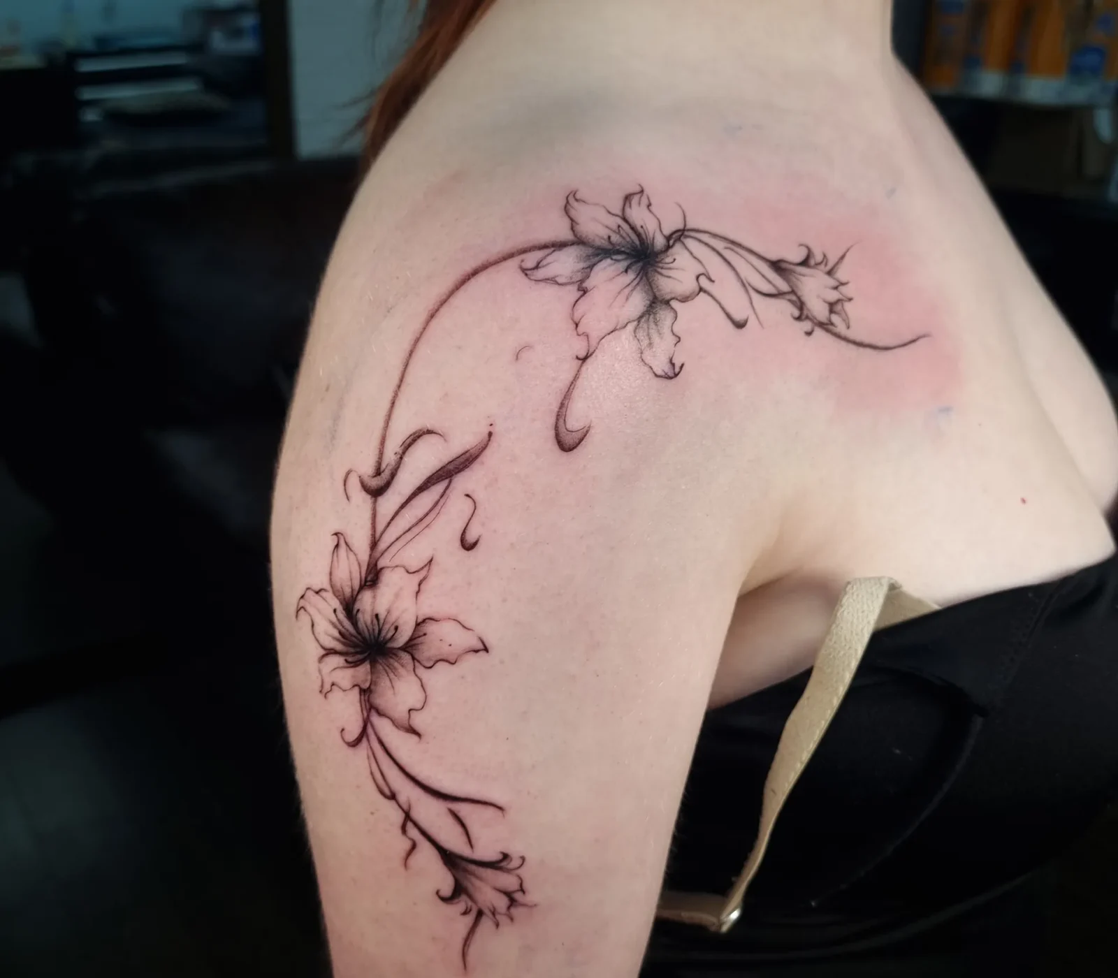 Fine-line floral tattoo flowing across the shoulder and upper arm