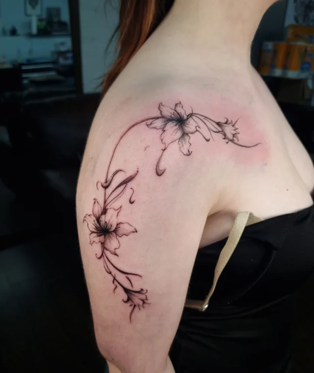 Fine-line floral tattoo flowing across the shoulder and upper arm