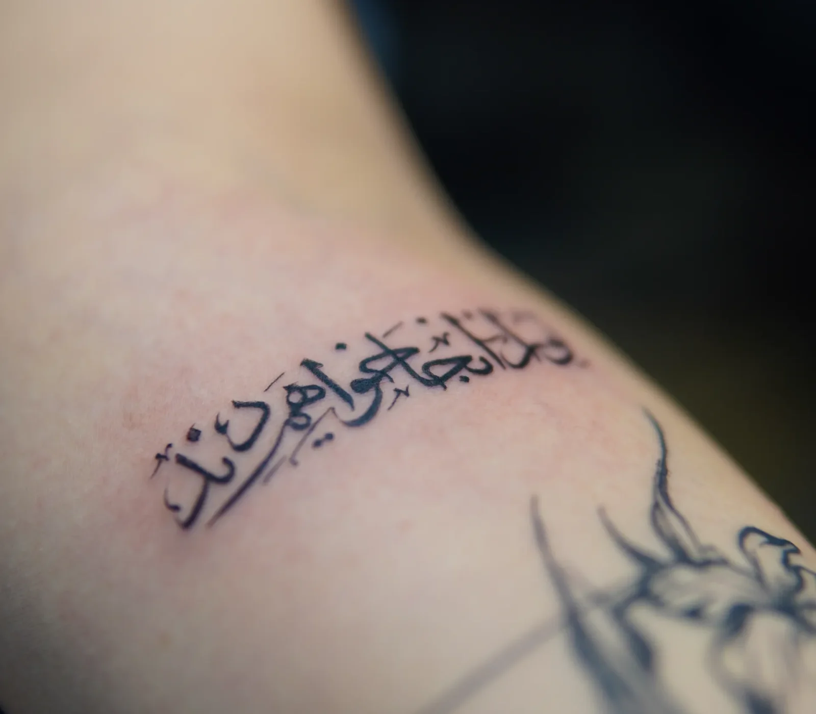 Fine-line Persian calligraphy tattoo in black ink on the forearm