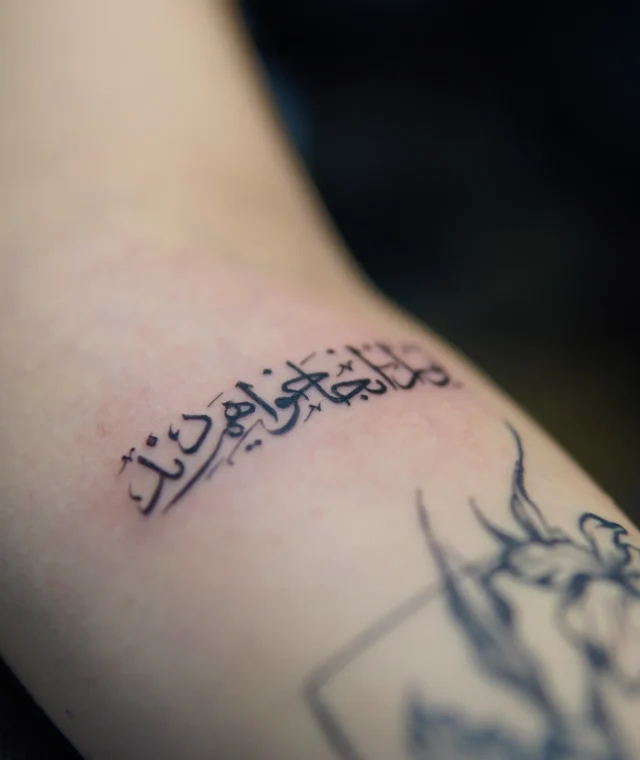 Fine-line Persian calligraphy tattoo in black ink on the forearm