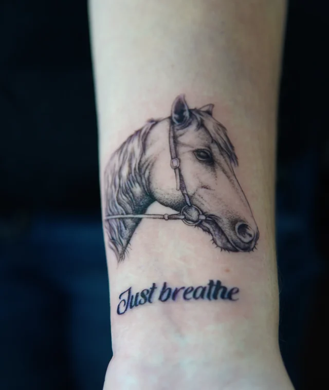 Horse portrait and “Just breathe” lettering tattoo on the forearm
