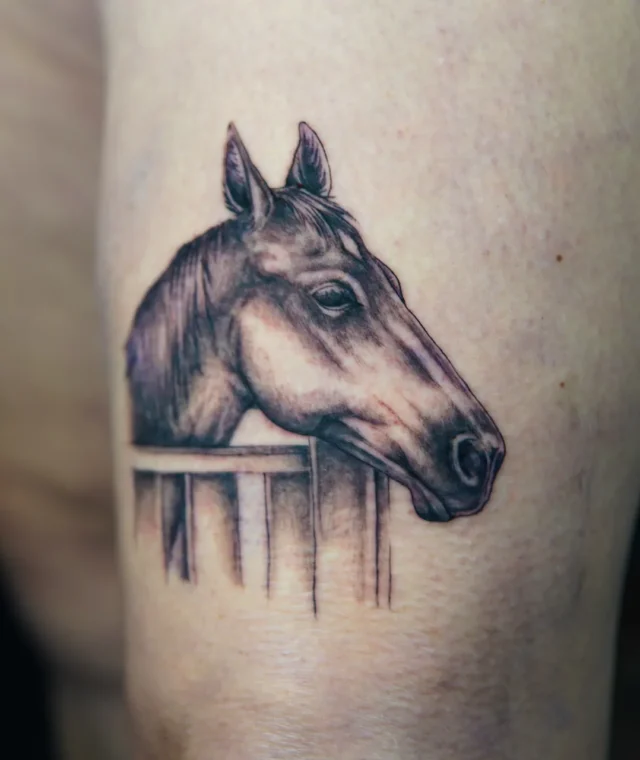 Realistic black-and-grey horse head tattoo on the thigh